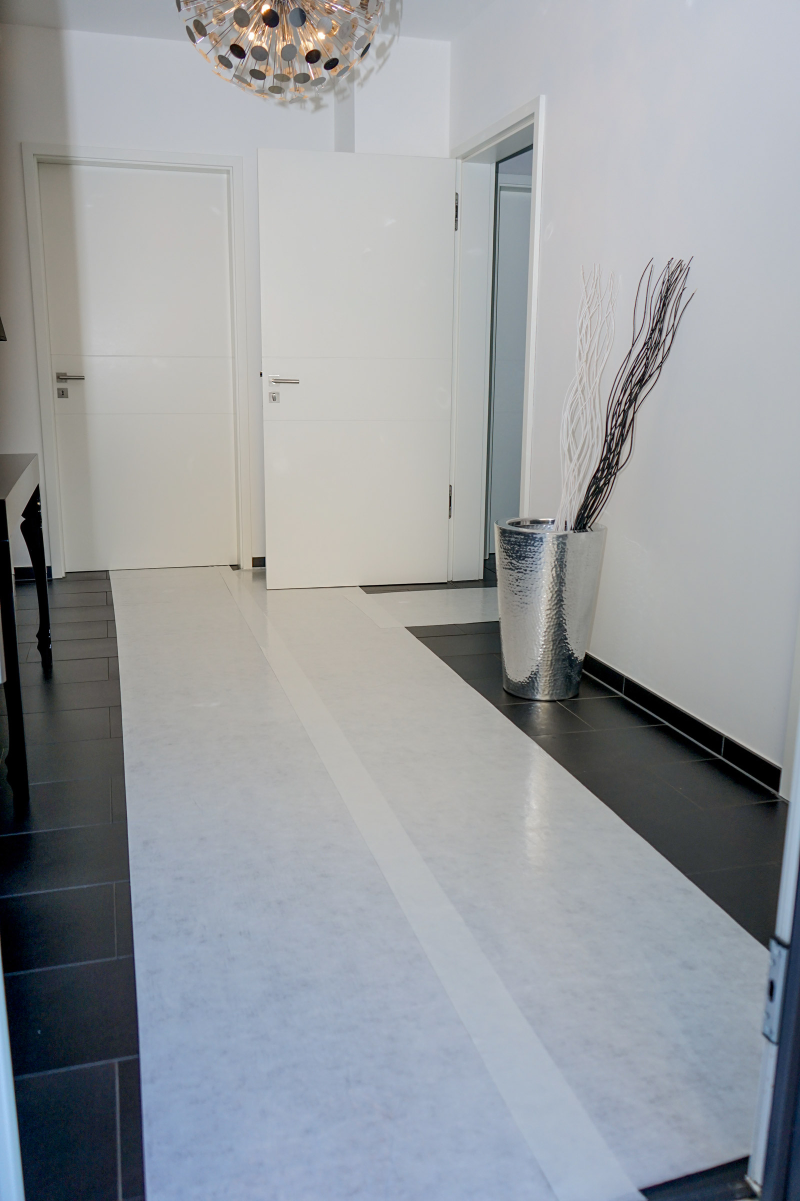 Heller Flur mit dunklen Fliesen, die mit einer selbstklebenden Abdeckfolie zum Schutz des Bodens während Renovierung abgedeckt sind