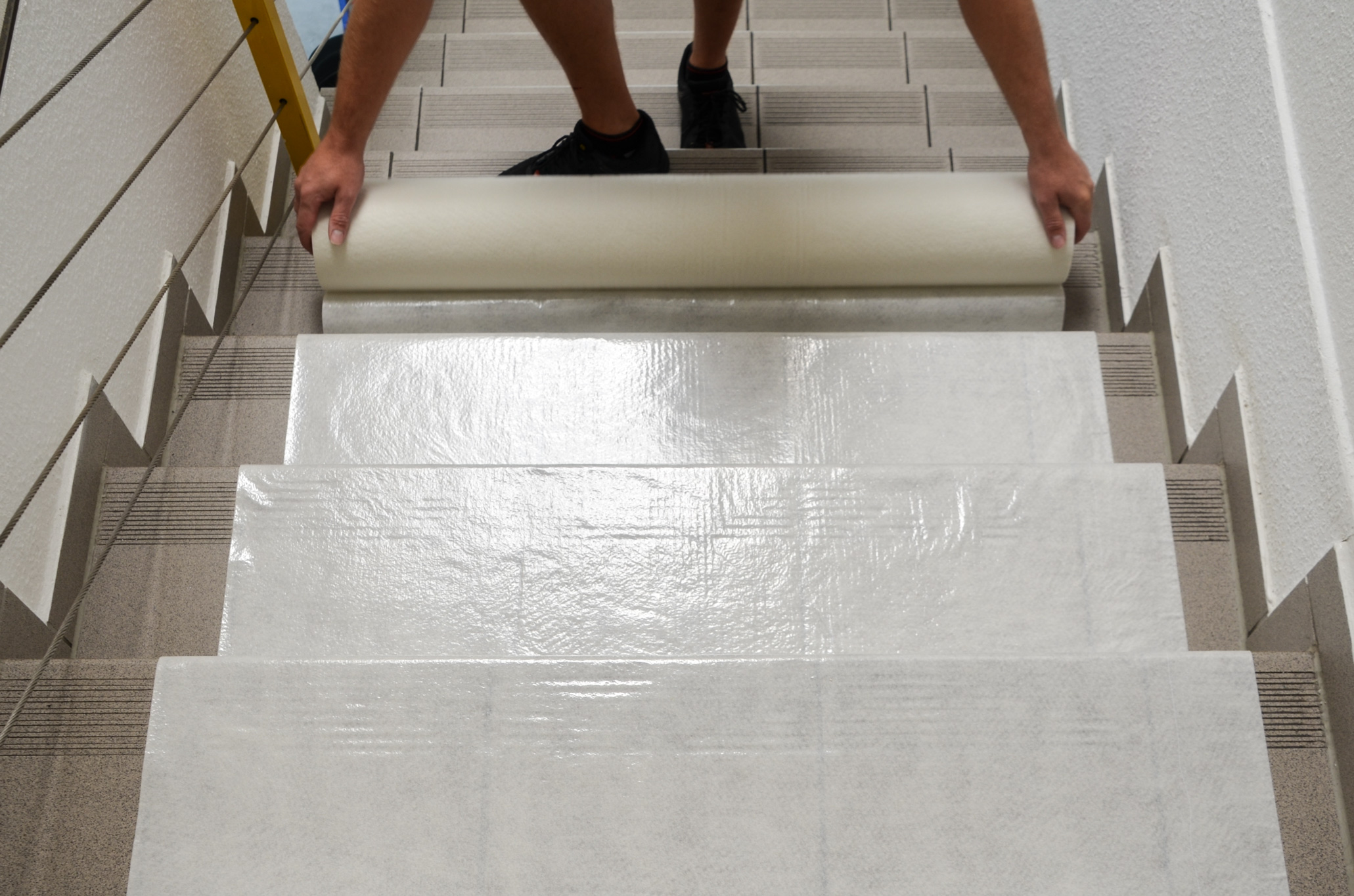 Person rollt selbstklebende Schutzfolie auf einer Treppe aus, um die Stufen während Bau- oder Renovierungsarbeiten zu schützen