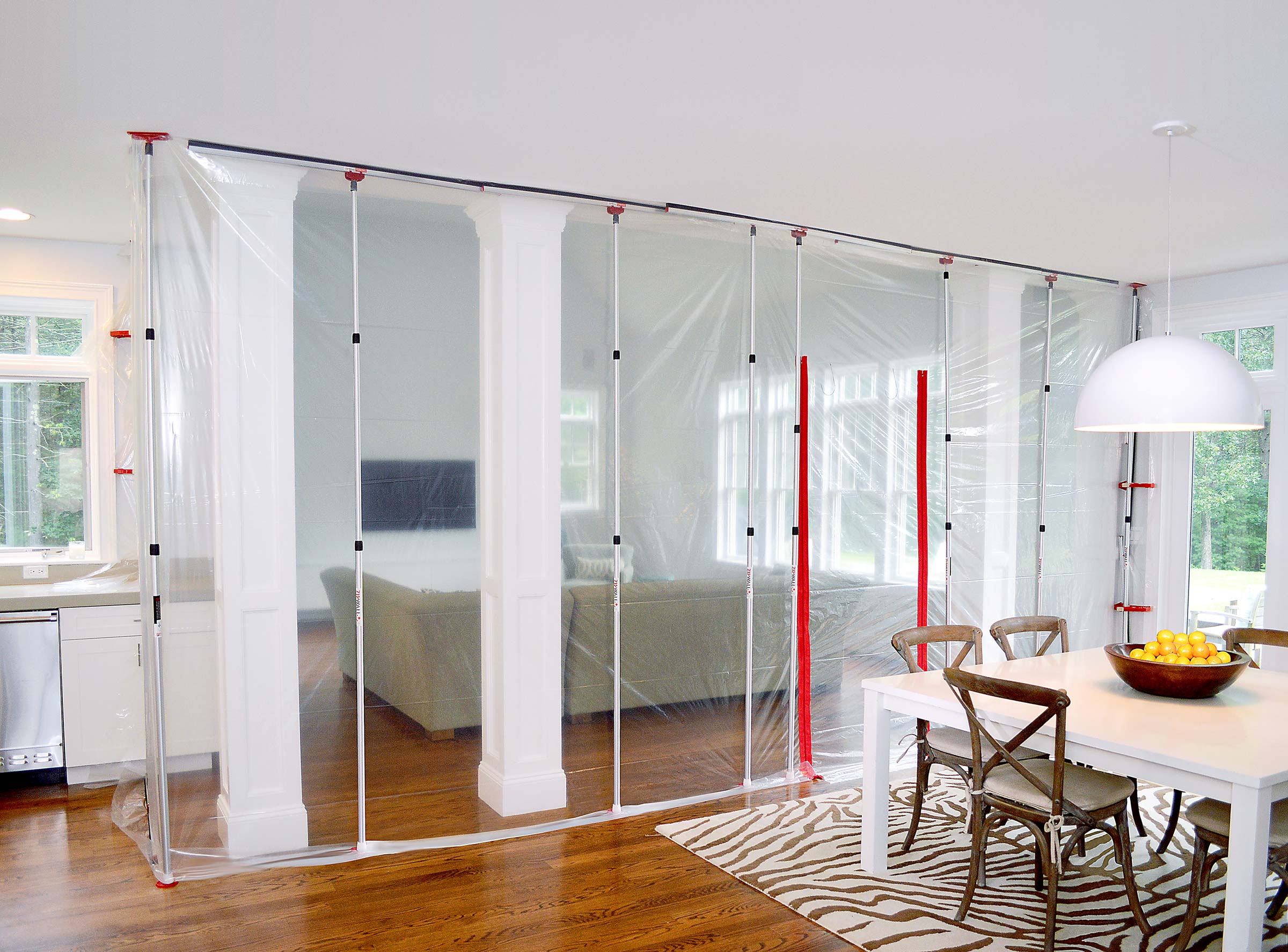 Transparente Staubschutzwand mit Folie und Teleskopstangen trennt während Renovierung den Wohnbereich vom Essbereich in einem modernen Haus