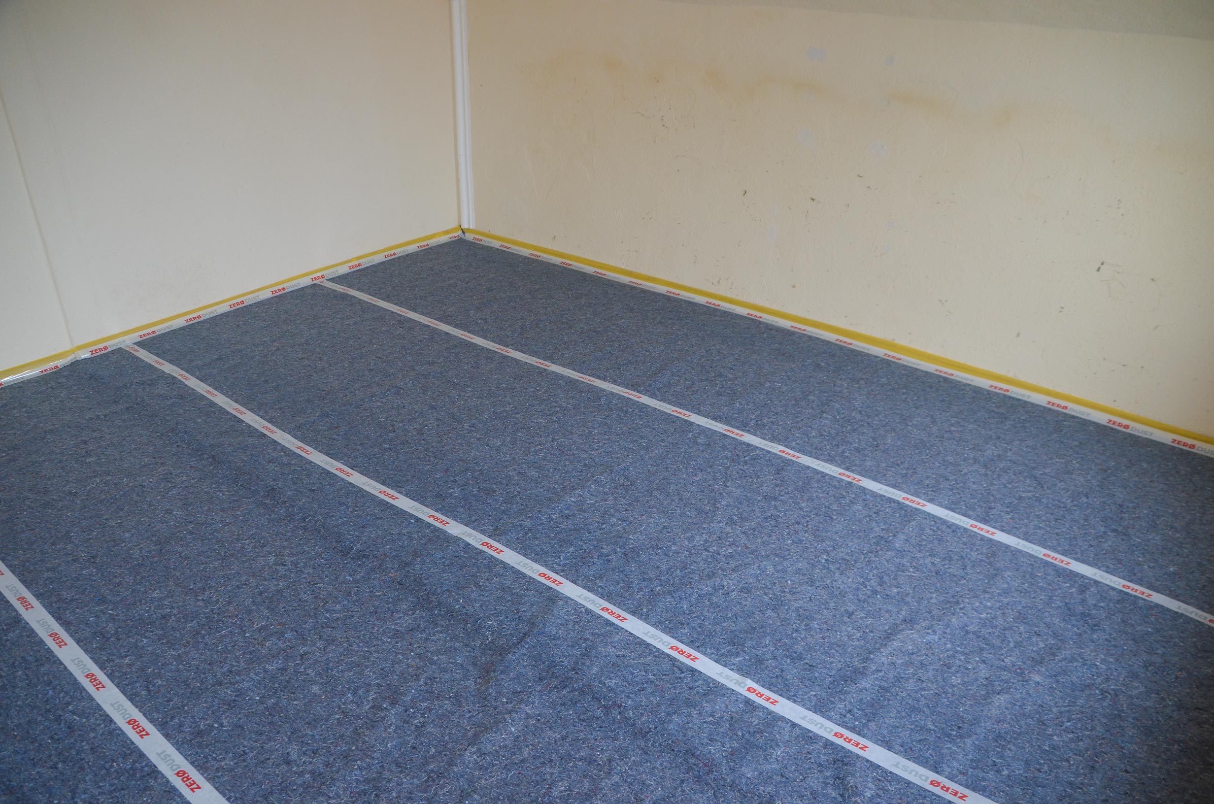 Boden eines leeren Raumes mit vollflächig verlegter Filz-Trittschalldämmung, mit Klebeband fixiert, als Unterlage für Laminat- oder Parkettboden