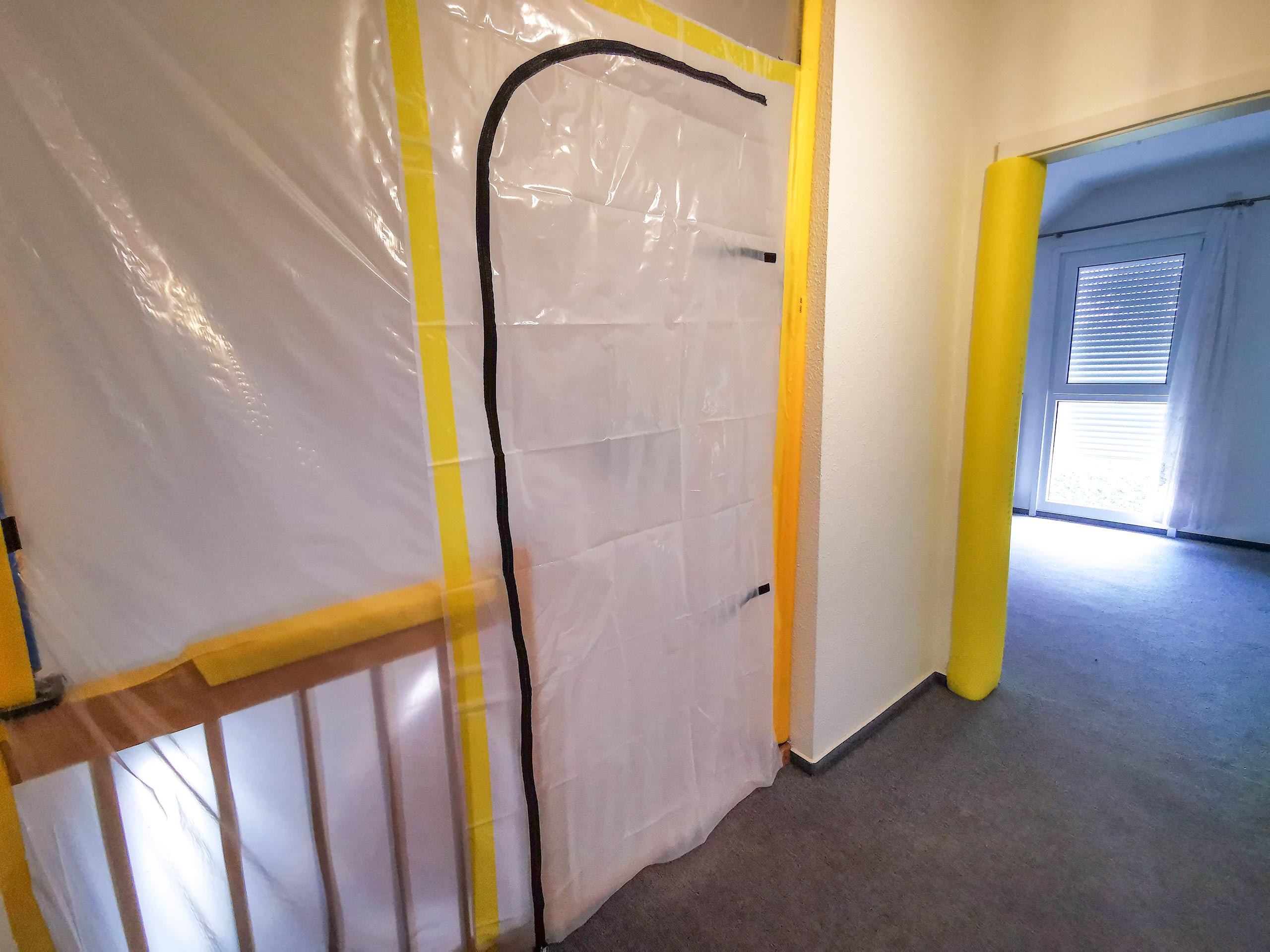 Eingebaute Staubschutztür aus transparenter Folie mit Reißverschluss, mit gelbem Klebeband im Türrahmen befestigt, als Staubschutz bei Renovierungsarbeiten in einer Wohnung