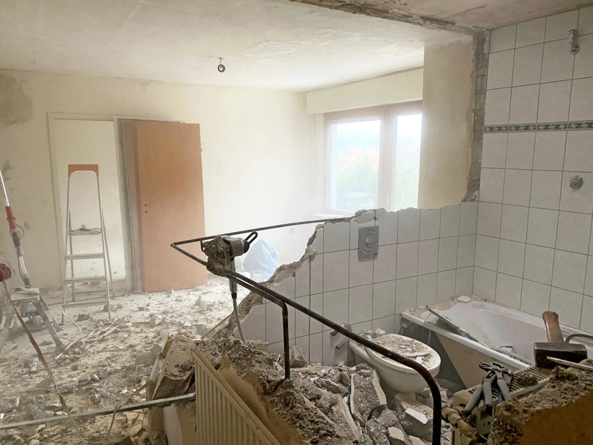 Staubige Baustelle beim Wohnungsumbau, altes Badezimmer mit herausgerissener Wand, freigelegener Badewanne, Toilette und Bauschutt auf dem Boden