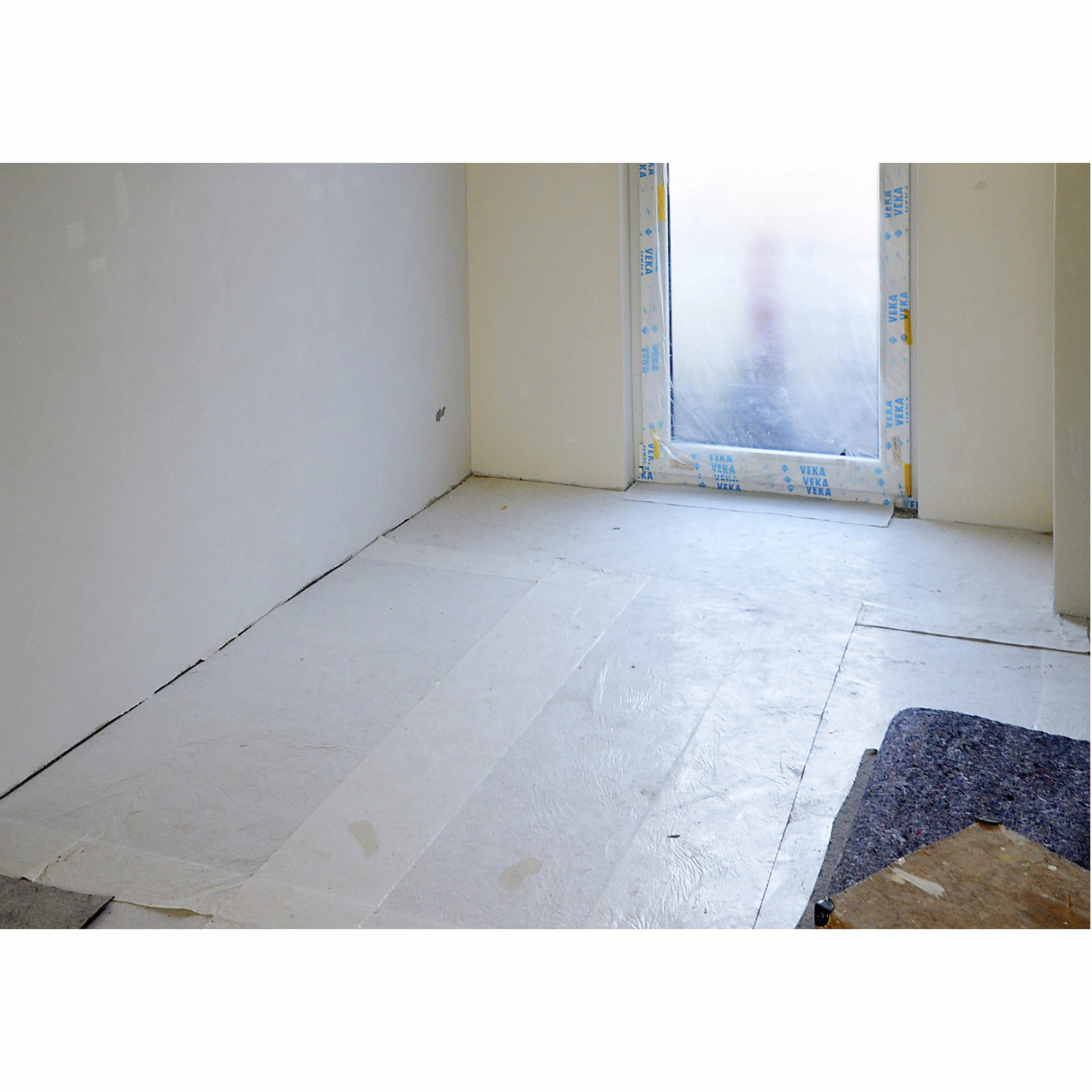 Mit Abdeckvlies ausgelegter Boden als Schutz bei Renovierungsarbeiten in einem hellen Raum mit Fenster