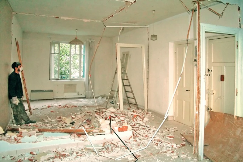 Bausanierung in einer Wohnung mit entfernten Innenwänden, herumliegendem Bauschutt und Handwerker mit Atemschutzmaske