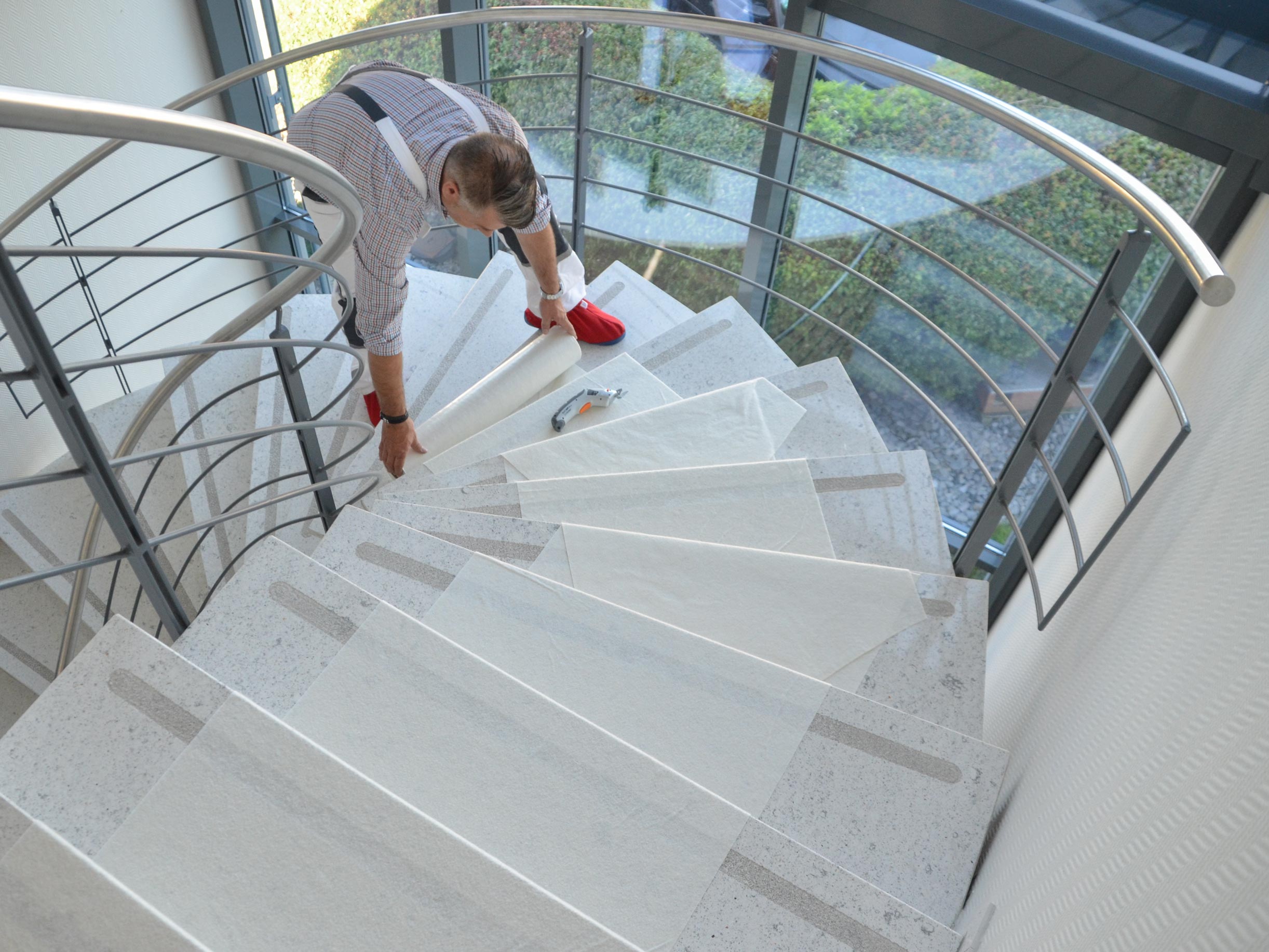 Handwerker bringt selbstklebendes Treppenschutz-Vlies auf einer modernen Innentreppe an, um Stufen während Renovierung und Malerarbeiten zu schützen