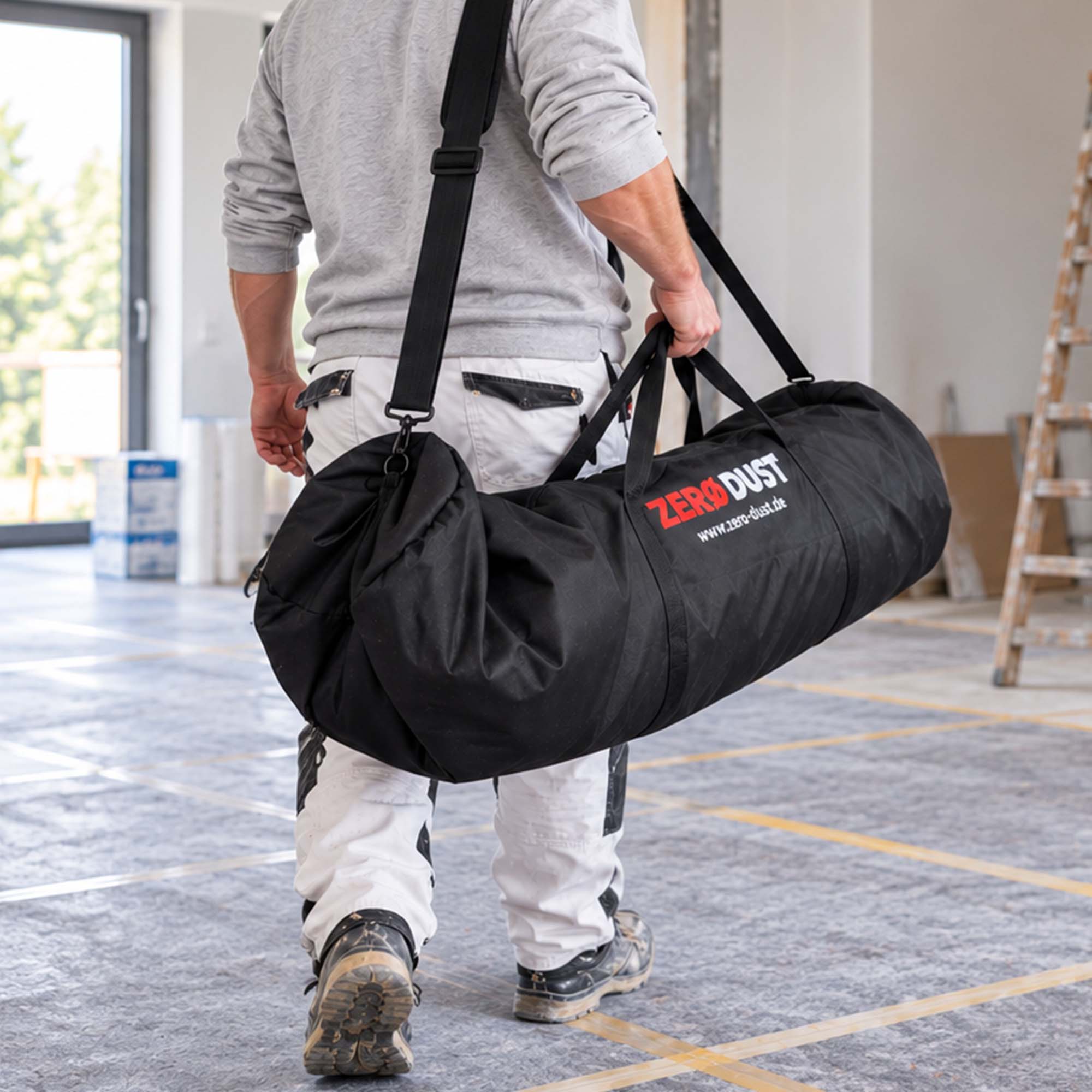 Handwerker trägt die Zero Dust MalerMuli Transporttasche für Vliesrolle bis 1,00 x 50 m sowie Klebeband, Cutter und Zubehör in einem renovierten Raum