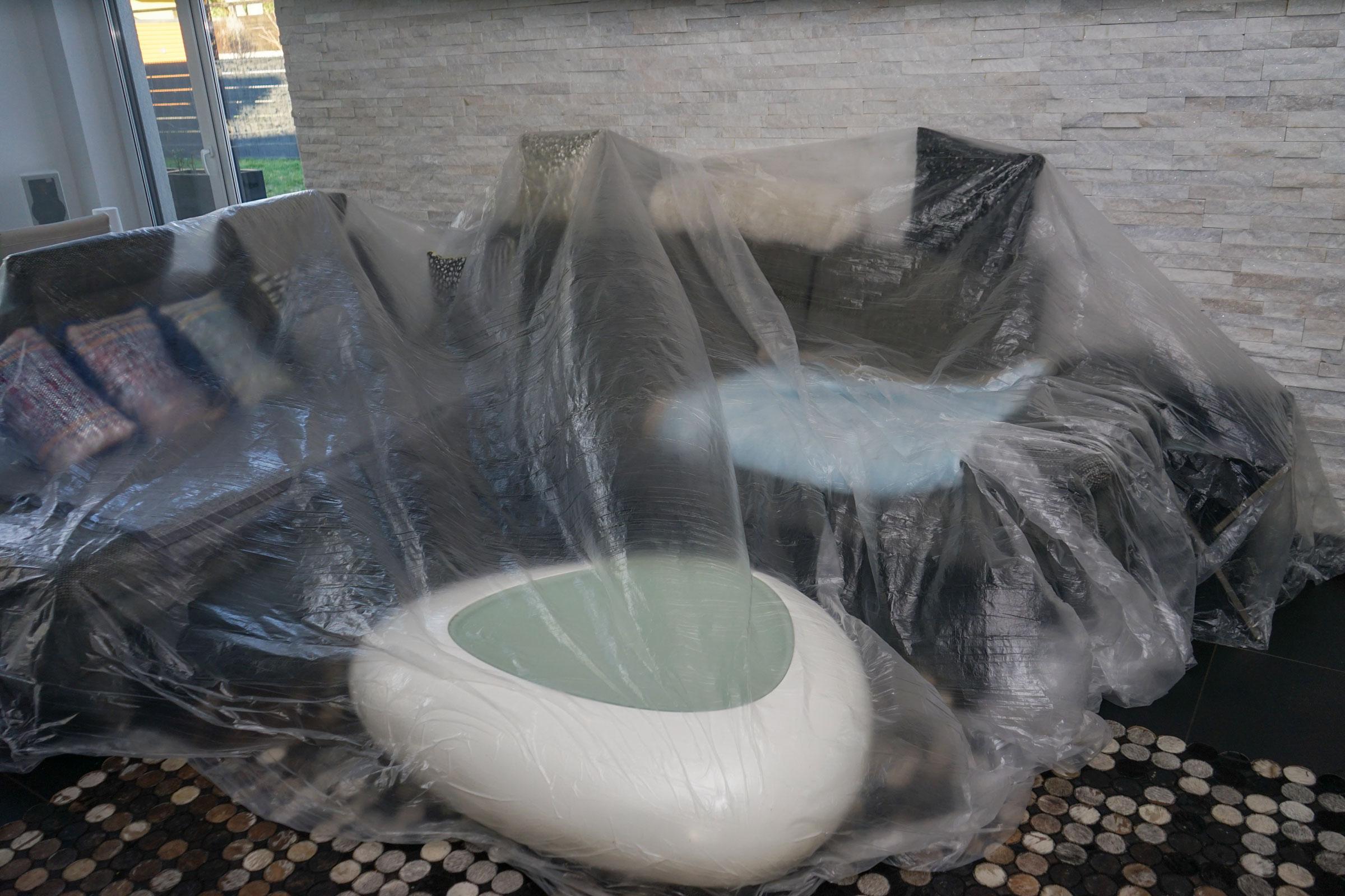 Wohnzimmermöbel, darunter Sofas und ein moderner Couchtisch, sind mit einer großen transparenten Schutzfolie zum Schutz vor Staub und Schmutz abgedeckt