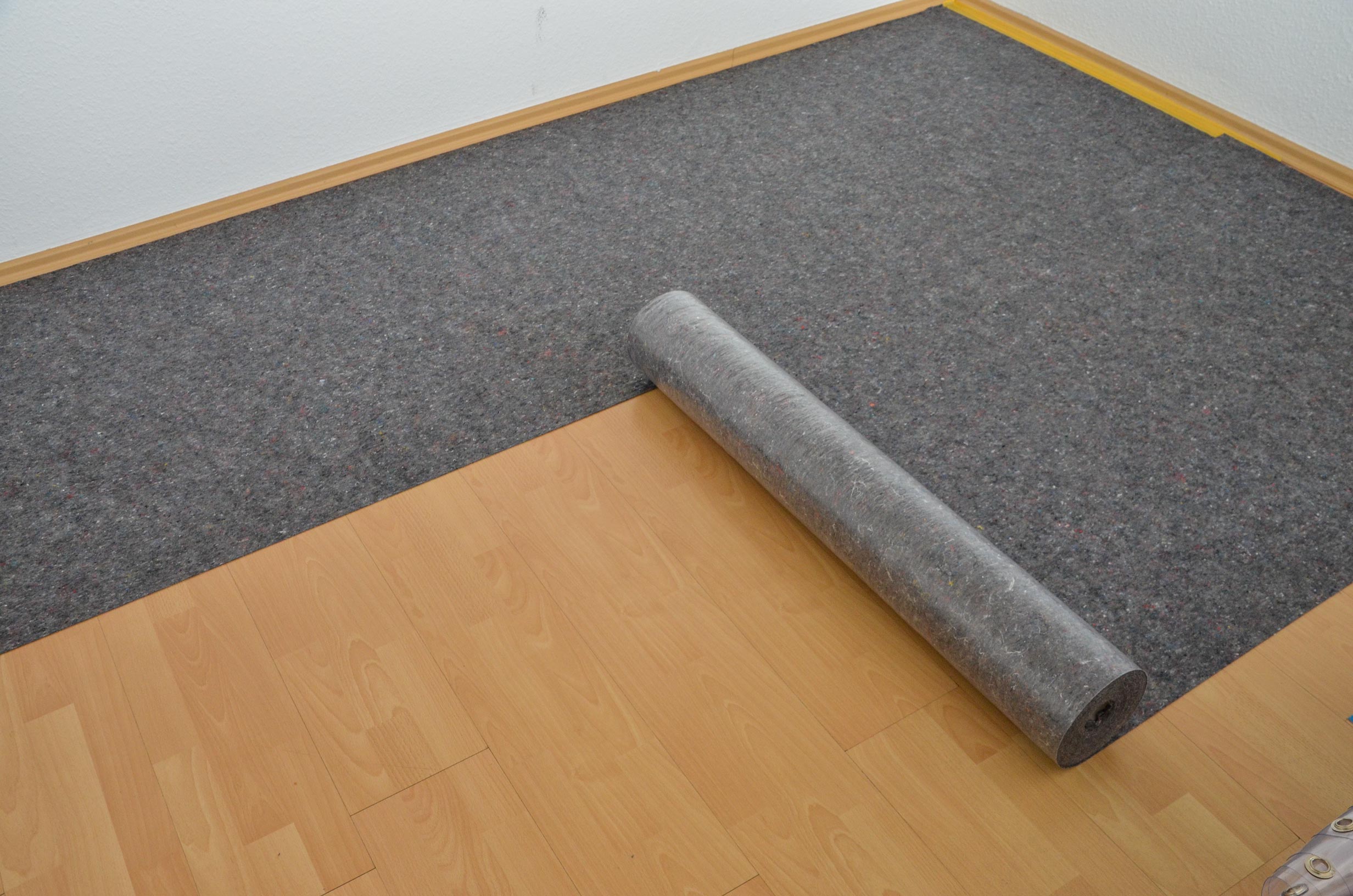 Graue Filz-Trittschalldämmung als Bodenunterlage, ausgerollt auf hellem Laminatboden entlang der Wand
