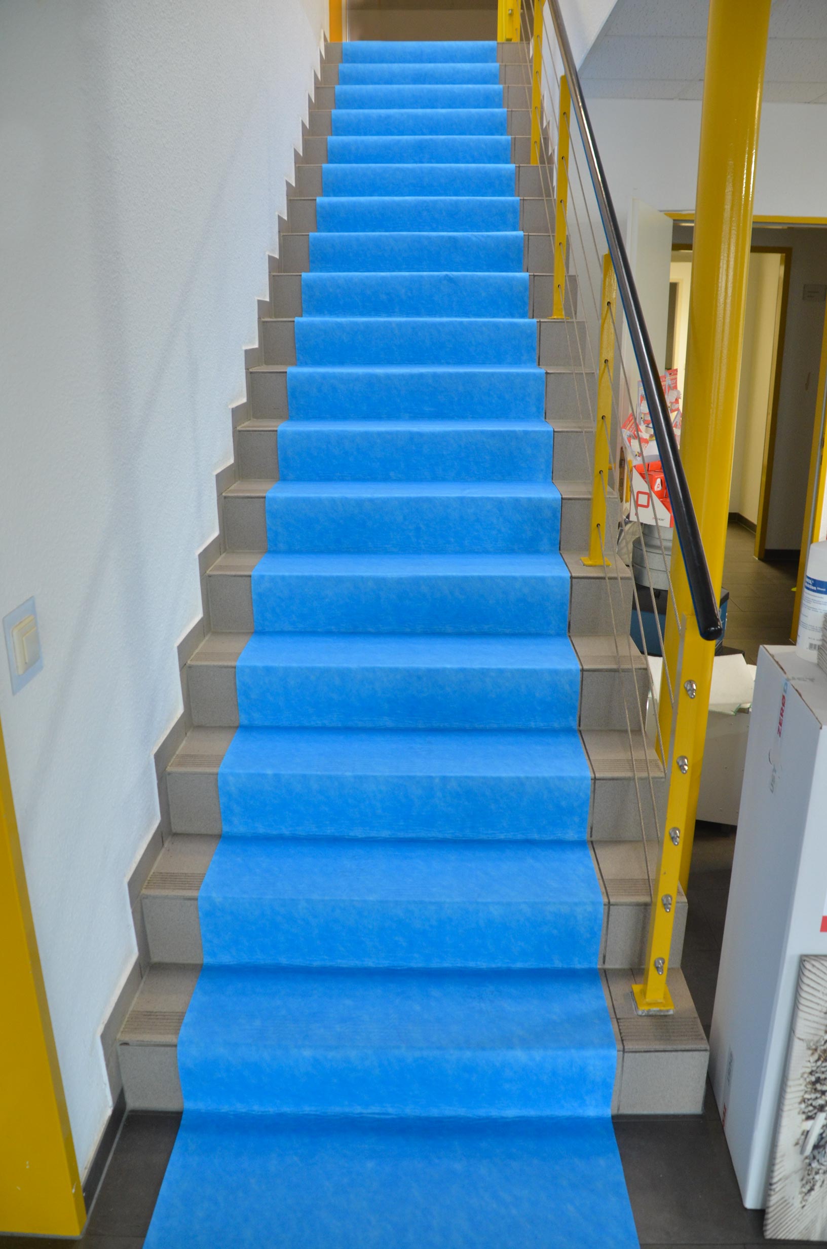 Innenraumtreppe mit blauem Treppenschutzvlies als rutschfeste Abdeckung der Stufen während Renovierungsarbeiten