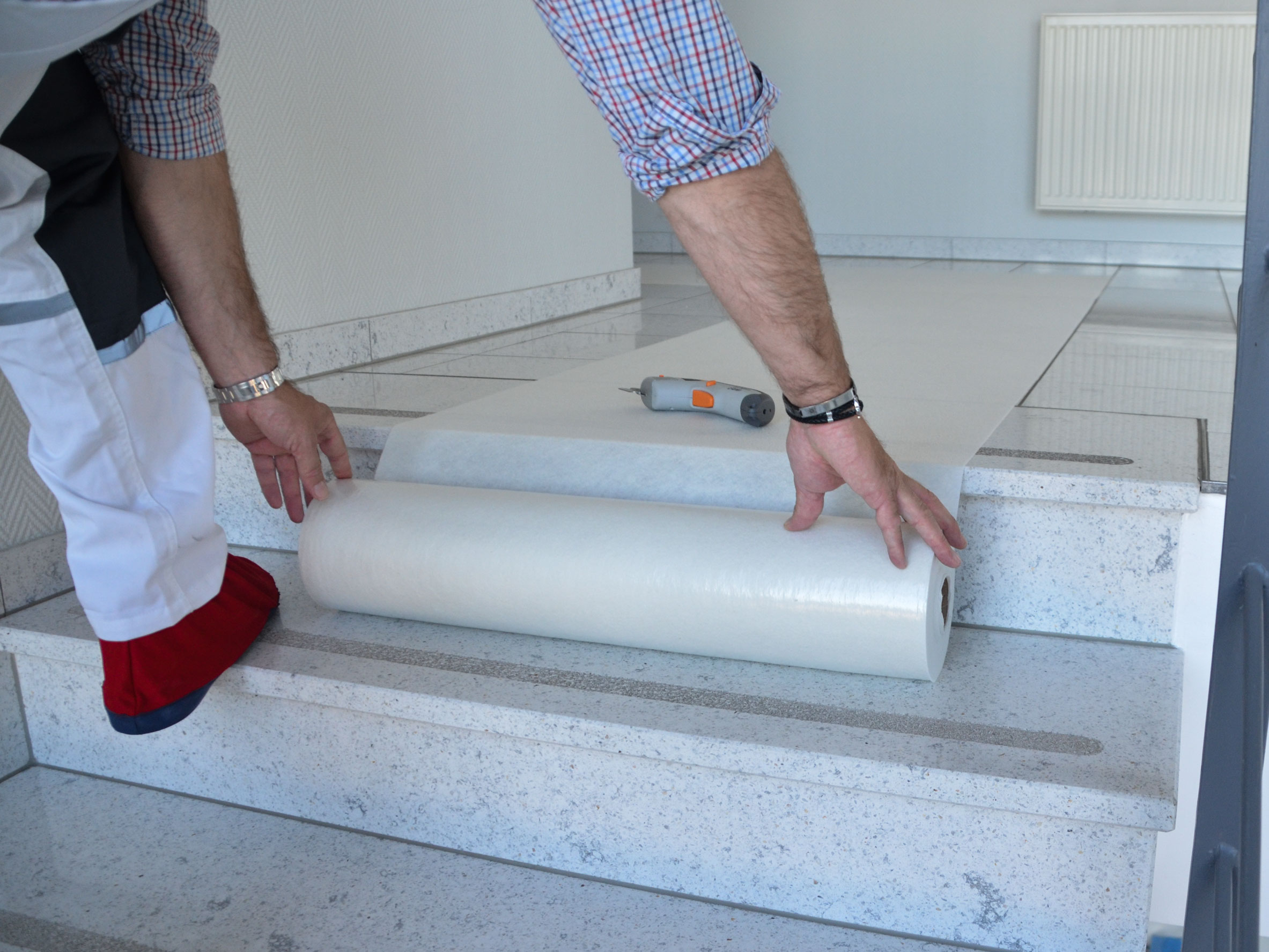Handwerker rollt eine schützende Abdeckfolie auf einer Steintreppe aus, um die Stufen während Renovierungsarbeiten zu schützen