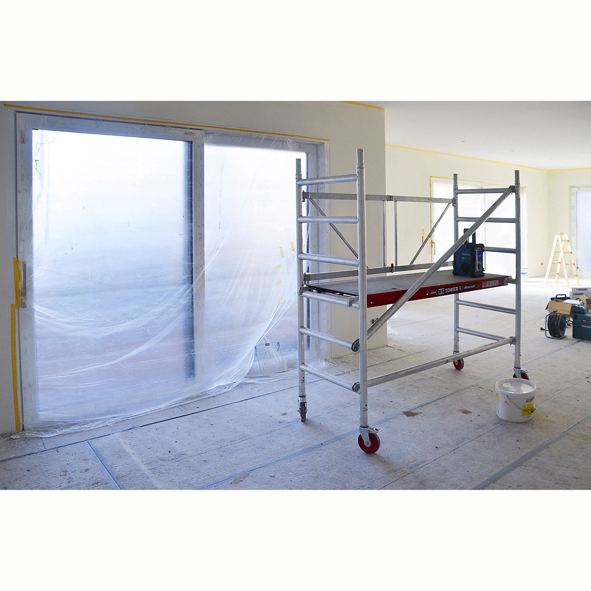 Mobiles Aluminium-Arbeitsgerüst mit Rollen in einem renovierten Innenraum mit abgedeckten Fenstern und Werkzeugen