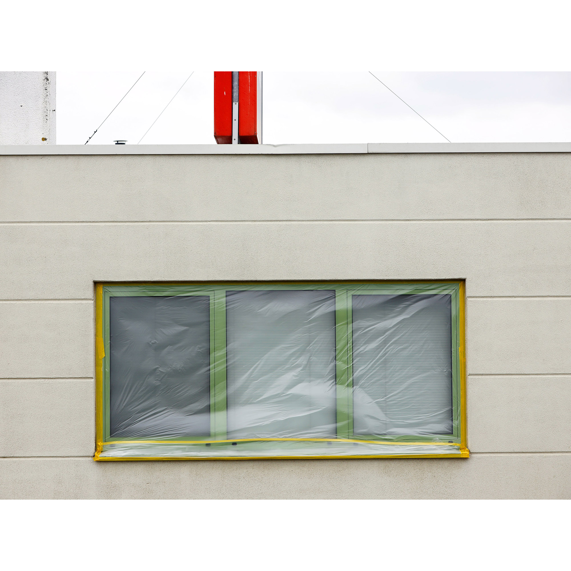 Rechteckiges Fenster an einer hellen Hausfassade, komplett mit Folie, Kreppband und Abklebung für Maler- oder Renovierungsarbeiten geschützt