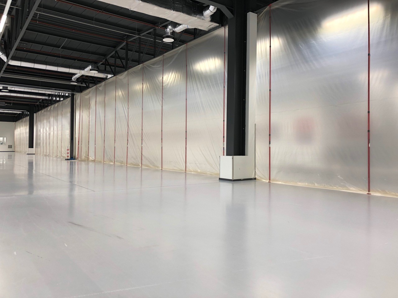 Leere Industriehalle mit glattem Betonboden und durchsichtigen Staubschutzwänden zur temporären Abtrennung des Arbeitsbereichs