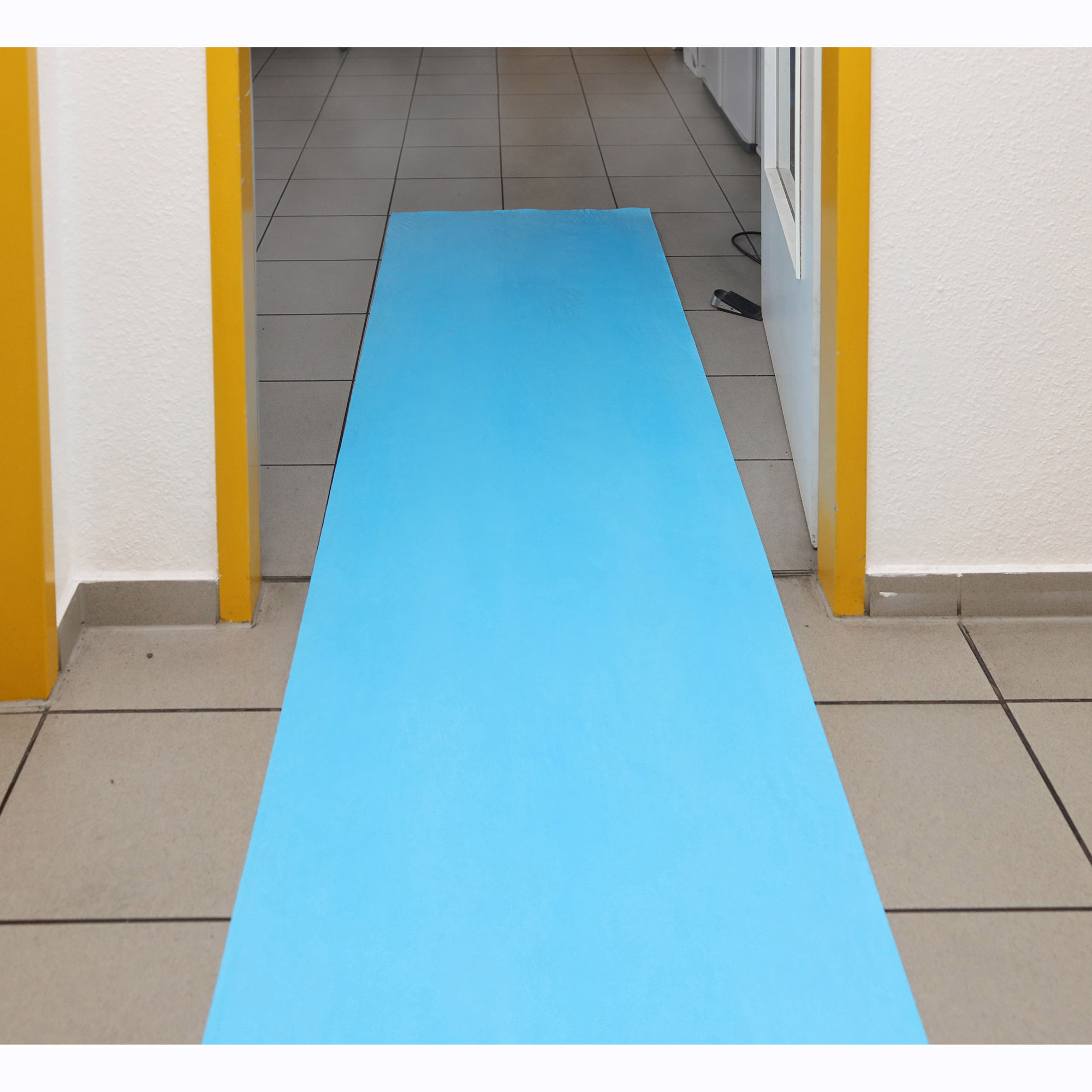 Blaue, rutschhemmende Schutzfolie als temporäre Bodenabdeckung auf einem gefliesten Flur mit gelben Türrahmen