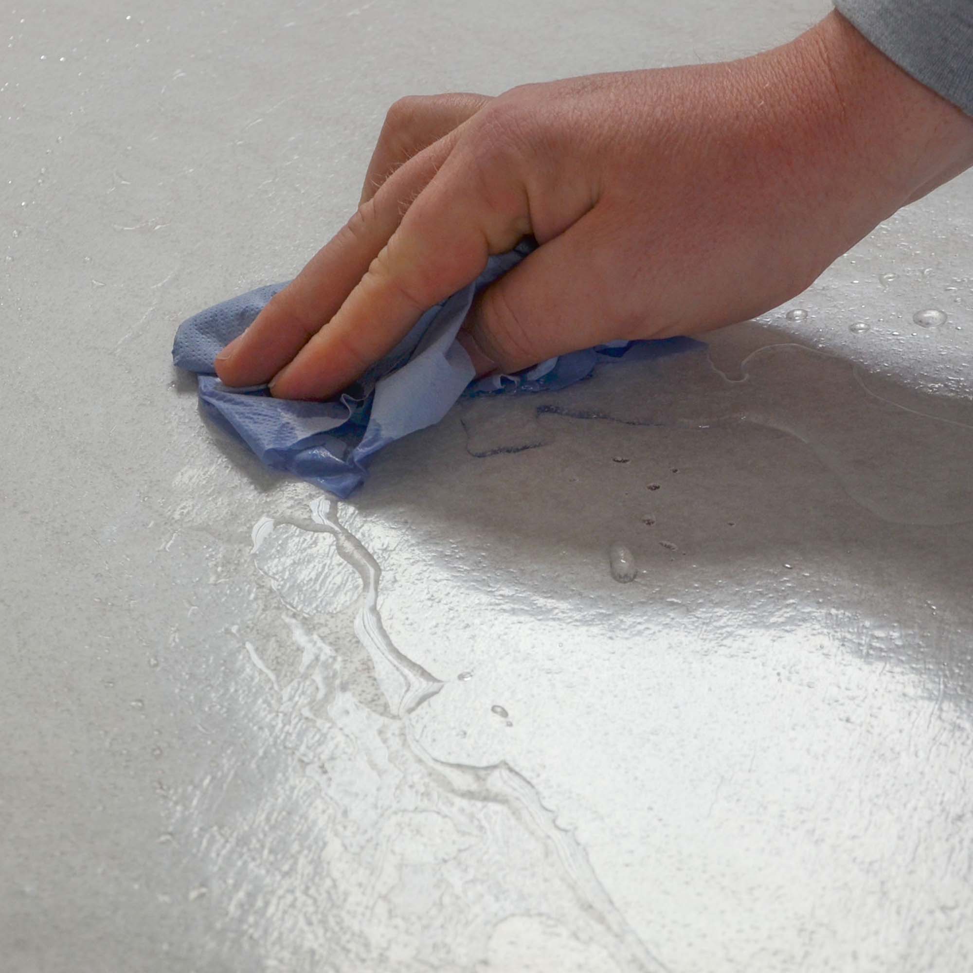 Hand wischt Wasser von der flüssigkeitsabweisenden Oberfläche des selbsthaftenden Zero Dust Treppenschutzvlies 160 g/m², weiß, 1,00 m x 25–50 m