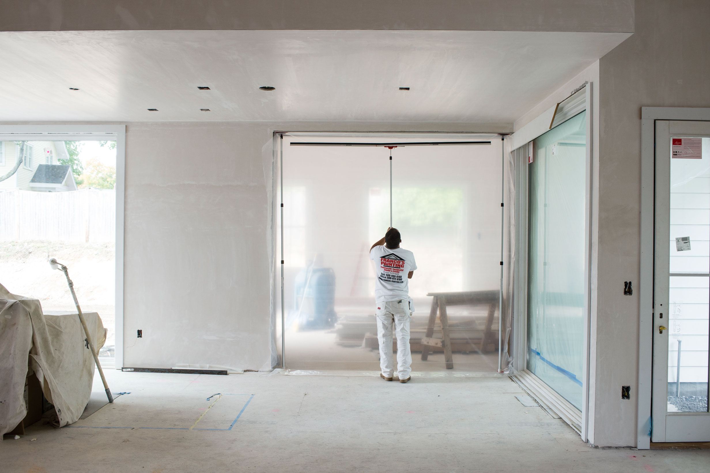 Handwerker montiert transparente Staubschutzfolie mit Reißverschluss in einer Türöffnung während Renovierungsarbeiten im Innenraum