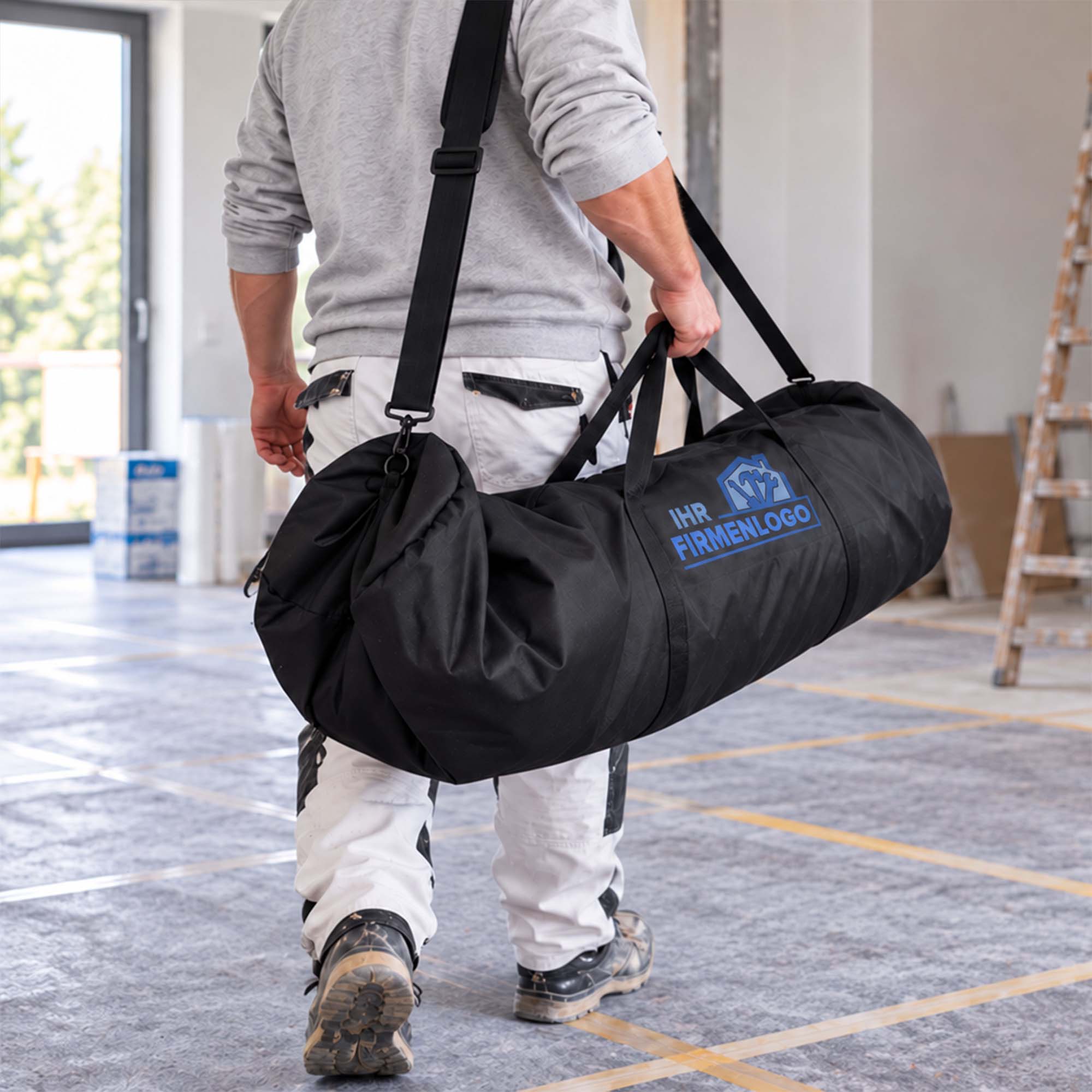 Handwerker trägt die Zero Dust MalerMuli Transporttasche für Vliesrolle bis 1,00 x 50 m und Zubehör mit Firmenlogo in einem renovierten Innenraum