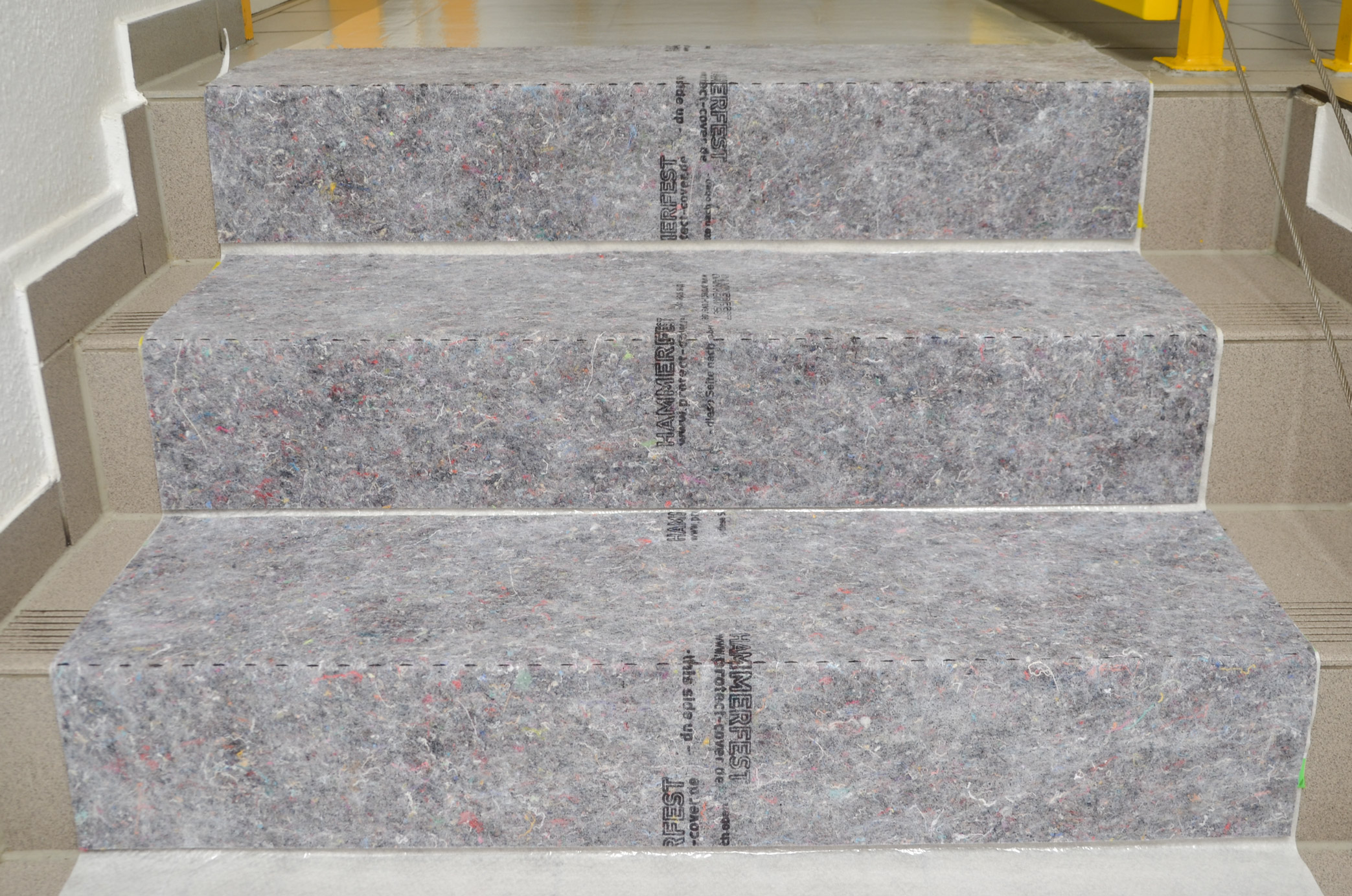 Mit grauem Schutzvlies vollständig abgedeckte Treppe als Stufenschutz zur sicheren, rutschhemmenden Abdeckung bei Renovierungsarbeiten
