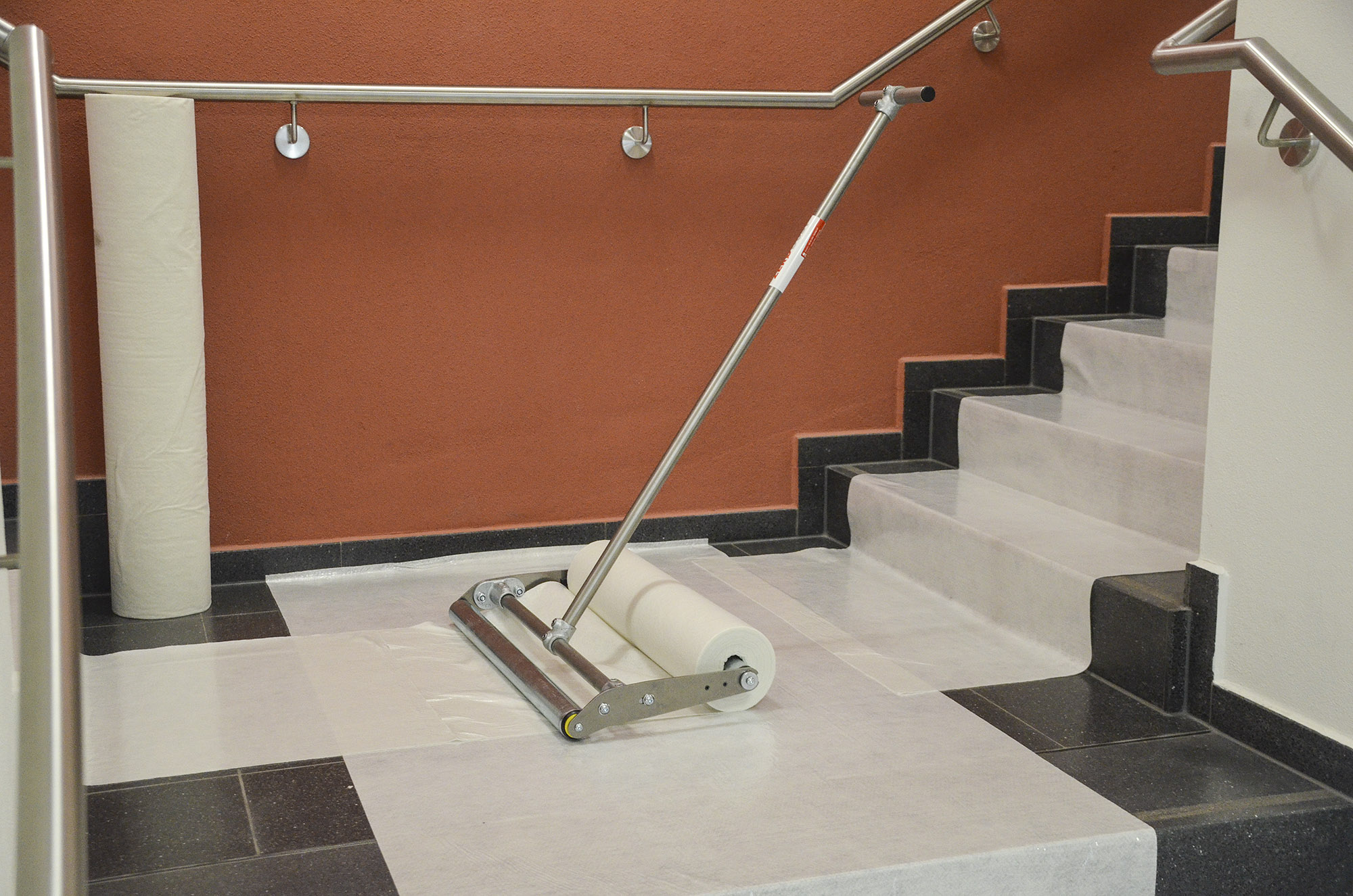 Treppenhaus mit verlegtem Schutzvlies auf Stufen und Podest, ausgerollt mit einem professionellen Abrollwagen für Bodenschutz beim Renovieren