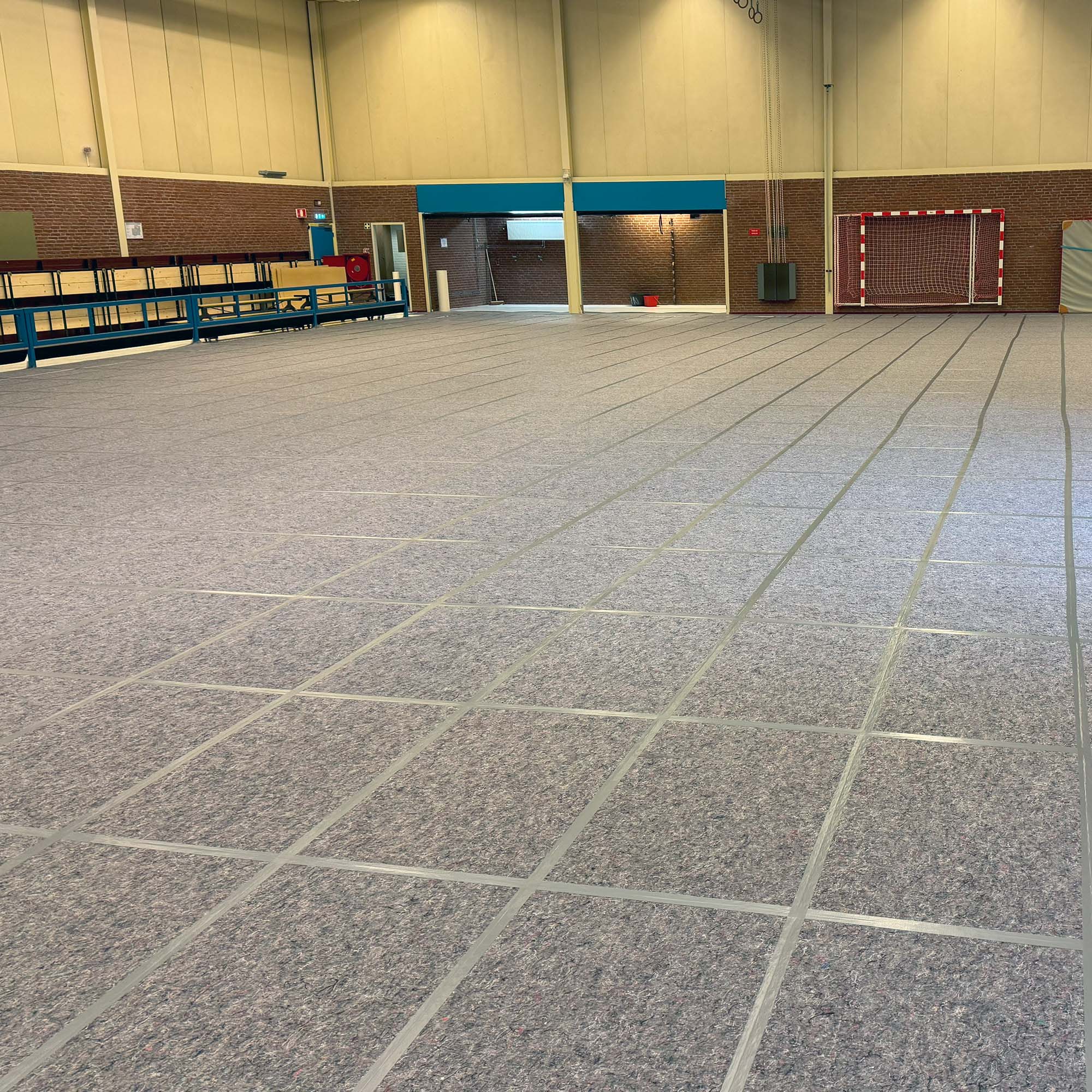 Große Sport- bzw. Mehrzweckhalle mit verlegtem Schutzboden aus grauen Teppichfliesen, die den Hallenboden vollständig abdecken