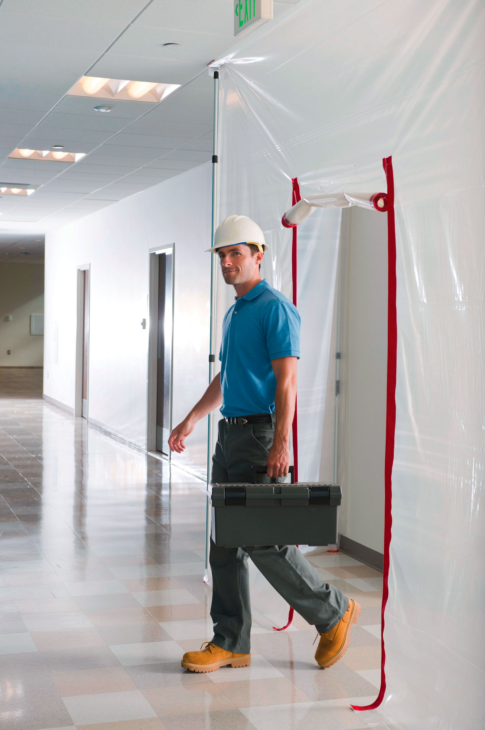 Handwerker mit Werkzeugkoffer geht durch transparente Staubschutztür mit Reißverschluss in einem Flur